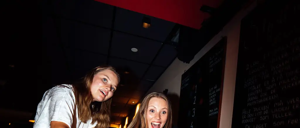 Glade gjester spiller shuffleboard under en sommerfest hos Oslo Bar & Bowling
